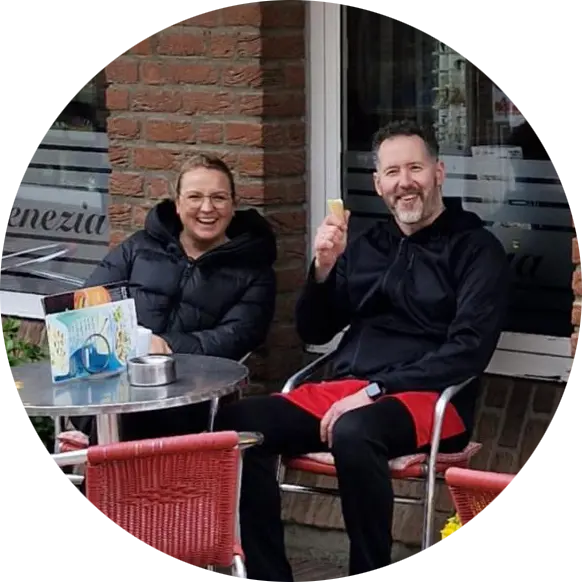 Melanie und Diego Altoe sitzen lachend an einem Tisch auf der Terrasse vor dem Café